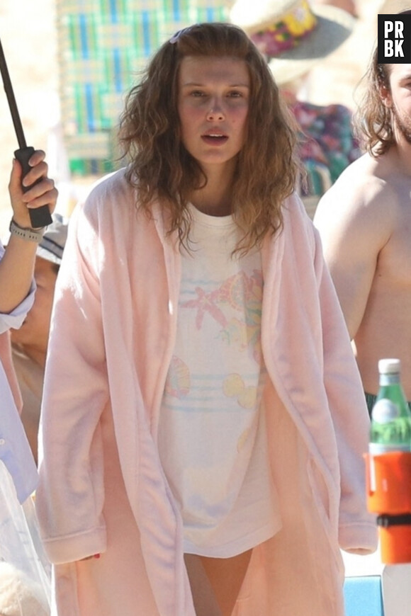 Exclusif - Millie Bobby Brown prend une pause (en peignoir rose) pendant le tournage de pour son prochain film "The Electric State" à Atlanta, Géorgie, Etats-Unis, le 24 octobre 2022.  Exclusive - Millie Bobby Brown covered up with a bathrobe and an assistant used an umbrella to walk her back to her tent after filming a beach scene for her next film 'The Electric State.' 