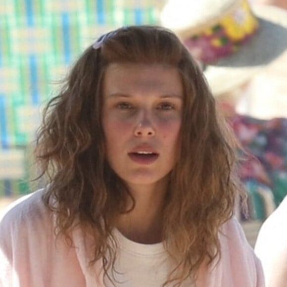 Exclusif - Millie Bobby Brown prend une pause (en peignoir rose) pendant le tournage de pour son prochain film "The Electric State" à Atlanta, Géorgie, Etats-Unis, le 24 octobre 2022.  Exclusive - Millie Bobby Brown covered up with a bathrobe and an assistant used an umbrella to walk her back to her tent after filming a beach scene for her next film 'The Electric State.' 