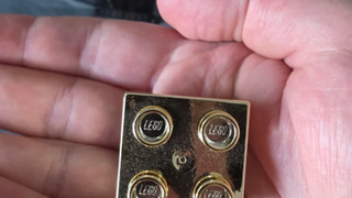 Un employé de LEGO montre ce qu'il a reçu pour son quatrième anniversaire : une brique Lego dorée que nous voulons tous avoir maintenant